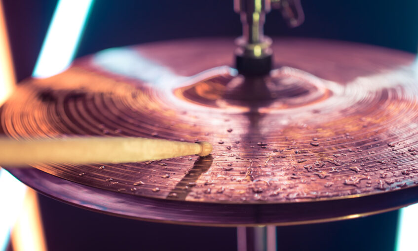 Hi-hat close-up of plates with drumsticks on a background of colored lanterns. Water drops on plates. Musical concept with a working drum.