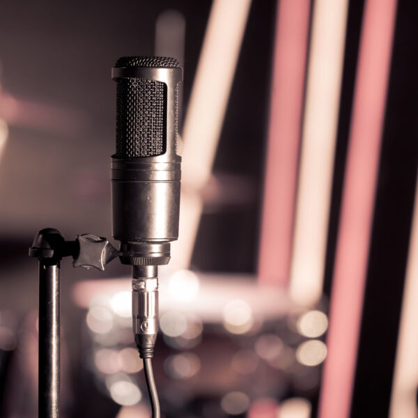 Microphone in recording Studio or concert hall close-up, with drum set on background out of focus. Beautiful blurred background of colored lanterns. Musical concept in vintage style.